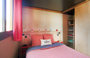 Acogedor dormitorio en una cabina Roulotte en Huttopia Les Châteaux, Francia, con detalles en rojo y luz.