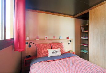 Chambre chaleureuse dans une roulotte à Huttopia Les Châteaux, France, décorée de rouge et baignée de lumière.