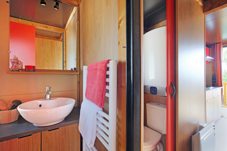 Modern cabin bathroom at Roulotte, Huttopia Les Châteaux in France, showing sink, mirror and toilet.