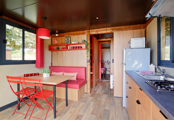 Moderne Glamping-Unterkunft mit Küchenzeile, Essbereich, roten Stühlen und viel Tageslicht.