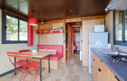 Modern glamping accommodation featuring a kitchenette, dining table with red chairs and large windows.