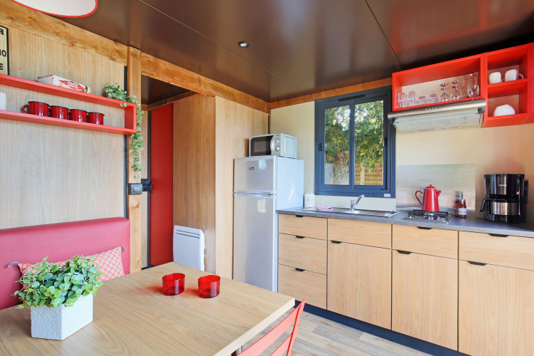 Modern kitchen and dining area inside a Roulotte cabin at Huttopia Les Châteaux, France, featuring red decor.