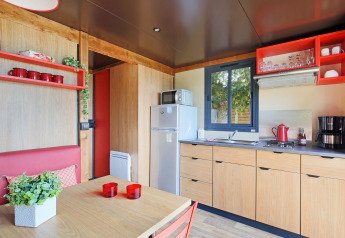 Cuisine moderne et coin repas dans une roulotte à Huttopia Les Châteaux, France, avec une décoration rouge et bois.