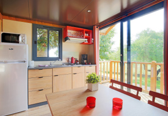 Modern kitchen and dining table in a cabin at Huttopia Les Châteaux, France, with view of greenery through windows.