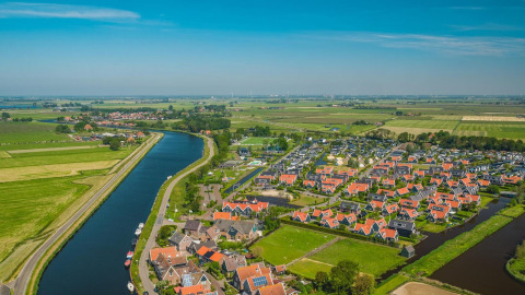 Luftfoto af Tiny House-lodge ved De Rijp i Holland med rødtage, kanal og grønne marker omkring.