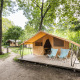 Classic safari tent with a wooden deck and two chairs, surrounded by trees in a forested campsite area.
