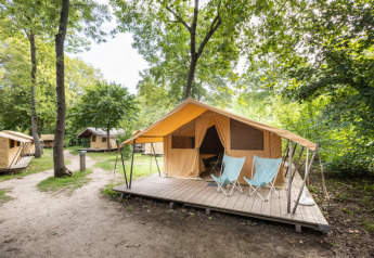 Tienda safari clásica con terraza de madera y dos sillas, ubicada en un camping rodeado de árboles.