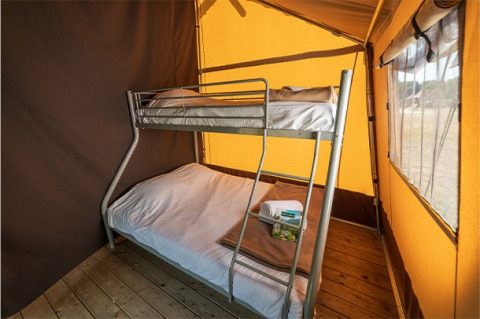 Stapelbed in het interieur van een klassieke safaritent op Camping de Paris, Frankrijk, met zonnig licht.