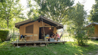 Safari teltet Tent Sweet står omgivet af træer med gæster, der slapper af på terrassen om sommeren.