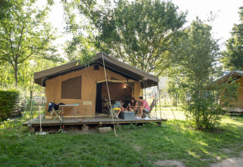 Tienda tipo safari Tent Sweet rodeada de árboles, con personas descansando en la terraza de madera.