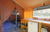 Binnenaanzicht van een safaritent met stapelbedden, keukenblok, koelkast en servies op Camping de Paris.
