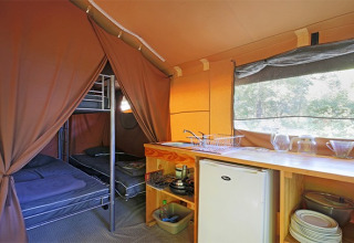 Vista interior de una tienda safari con literas, cocina, nevera y vajilla en Camping de Paris en Francia.