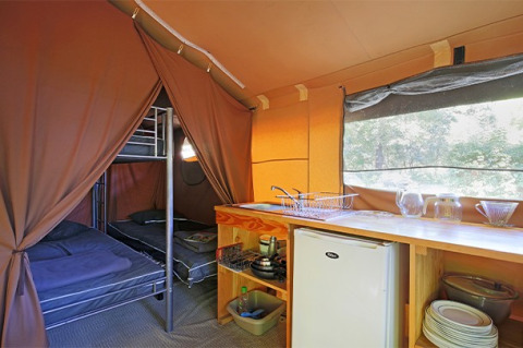 Vista interior de una tienda safari con literas, cocina, nevera y vajilla en Camping de Paris en Francia.