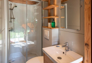 Baño moderno con ducha de vidrio, lavabo y espejo en una tienda safari en Camping de Paris, Francia.