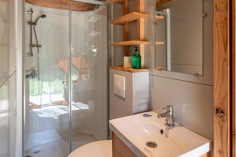 Baño moderno con ducha de vidrio, lavabo y espejo en una tienda safari en Camping de Paris, Francia.