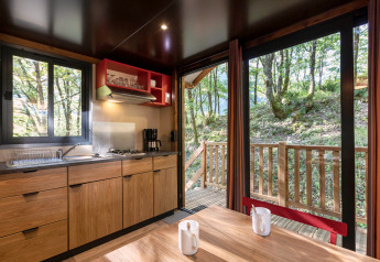 Vue intérieure d'une cuisine et table dans une roulotte au Camping de Paris, avec vue sur la forêt.
