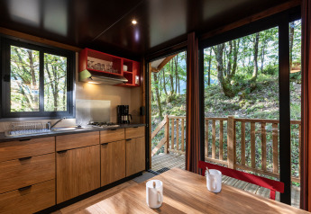 Vue intérieure d'une cuisine et table dans une roulotte au Camping de Paris, avec vue sur la forêt.