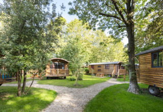 Gypsy caravan lodges in a lush, green setting at Camping de Paris in France, surrounded by trees and paths.