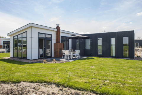 Modernes L-Pavilion-Ferienhaus bei Poort van Zeeland, Niederlande, mit Terrasse und großen Fenstern.