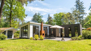 Lodge L-Pavilion moderno en un bosque verde, con terraza, mesa de comedor, sombrilla y caseta adicional.