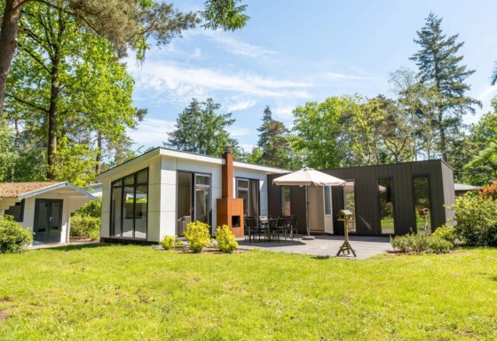Lodge L-Pavilion moderno en un bosque verde, con terraza, mesa de comedor, sombrilla y caseta adicional.