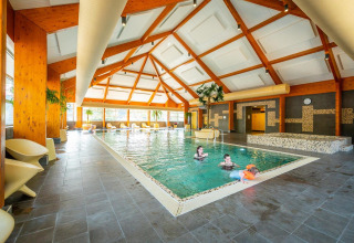 Indoor swimming pool at a glamping accommodation, with people enjoying the water under a high wooden ceiling.