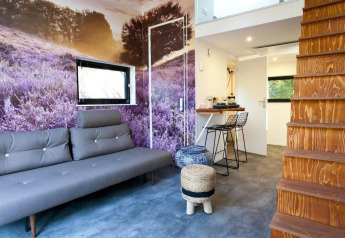 Modern tiny house interieur met lavendel muurfoto, grijze bank, houten trap en keukentje in Nederland.