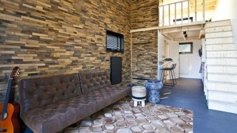 Sala de estar de tiny house moderna en De Zanding, Países Bajos, con pared de madera y sofá cómodo.