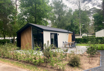Modern Berkel lodge surrounded by trees with a patio, outdoor dining set, and lush, green environment.