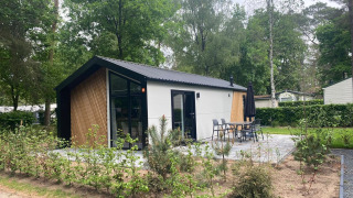 Moderne Berkel-lodge in een bosrijke omgeving met terras, tuinstoelen en veel natuurlijke begroeiing.