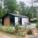 Moderne Berkel-lodge i skovområde med stor terrasse, havemøbler og grønne omgivelser i naturen.