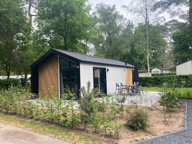 Modern Berkel lodge surrounded by trees with a patio, outdoor dining set, and lush, green environment.