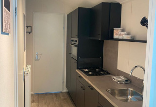 Cocina moderna y estrecha en un lodge Berkel de De Zanding, Países Bajos, con suelo de madera y gabinetes oscuros.