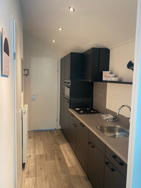 Modern narrow kitchen area in a Berkel lodge at De Zanding, Netherlands, with wood floor and dark cabinets.