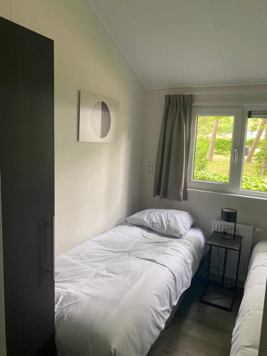 Bright lodge room with two single beds, white bedding, window view of greenery, and modern wall art at De Zanding.