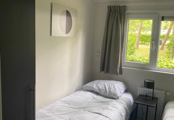 Chambre lumineuse avec deux lits simples, draps blancs, vue sur la verdure et art mural moderne à De Zanding.