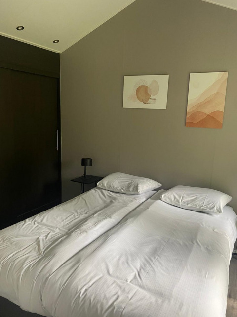 Dos camas individuales con sábanas blancas en un dormitorio moderno en Berkel lodge, De Zanding, Países Bajos.
