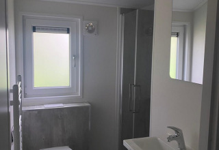 Baño moderno con inodoro suspendido, lavabo, espejo y ducha en la cabaña Berkel en De Zanding, Países Bajos.