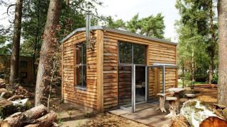 Een klein houten huisje genaamd Tiny House in het bos met grote ramen en boomstamzitplaatsen buiten.