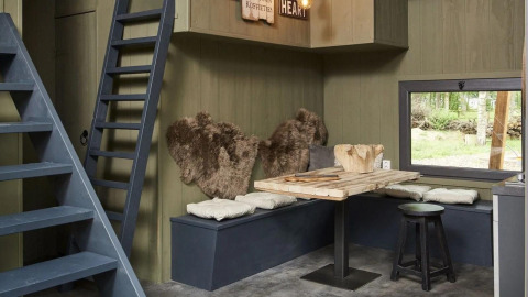 Interno del Tiny House a De Zanding, Paesi Bassi, con tavolo in legno, panche, cuscini e pelli.