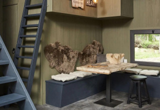 Interno del Tiny House a De Zanding, Paesi Bassi, con tavolo in legno, panche, cuscini e pelli.