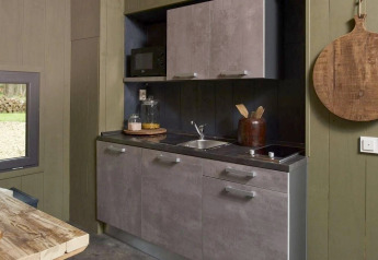 Moderne, kompakt køkkenhjørne i Tiny House ved De Zanding, Holland, med træbord og køkkenredskaber.