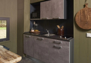 Modern, compact kitchenette in Tiny House at De Zanding, Netherlands, with wooden table and utensils visible.