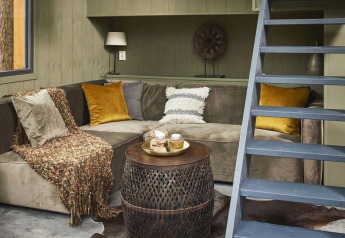 Knusse zithoek in het Tiny House bij De Zanding, Nederland, met hoekbank en open trap naar boven.
