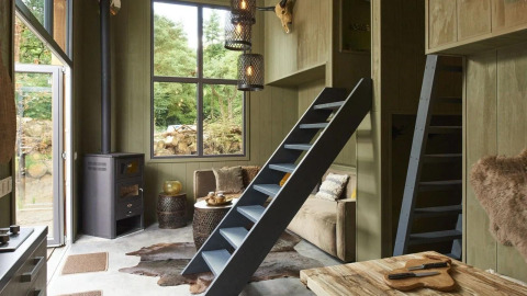 Interior de Tiny House en De Zanding, Países Bajos, con ventanas grandes, escaleras tipo loft y decoración cálida.
