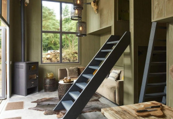 Intérieur d’un tiny house à De Zanding, Pays-Bas, avec grandes fenêtres, échelles et ambiance chaleureuse.