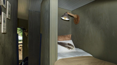 Vista interior de una cama acogedora y lámpara de pared en la Tiny House de De Zanding, Países Bajos.