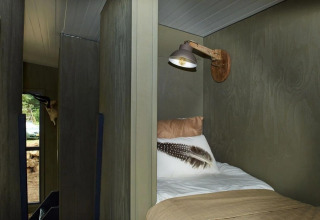 Vista interior de una cama acogedora y lámpara de pared en la Tiny House de De Zanding, Países Bajos.