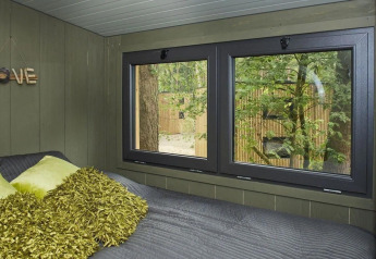 Acogedor dormitorio de tiny house con almohadas verdes, gran ventana y vista al bosque en De Zanding, Países Bajos.