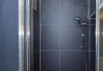 Moderne douche met donkere tegels in Tiny House bij De Zanding, Nederland, compact en stijlvol ingericht.